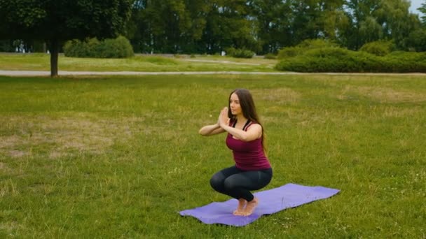 Mujer caucásica joven relajándose practicando yoga en el lugar al aire libre por la mañana. Hermosa mujer haciendo yoga en el parque en la hierba verde — Vídeos de Stock