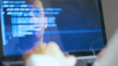 Bir dizüstü bilgisayarda çalışan Adam Hacker Programcı Çift Pozlama Shot. Monitörde Yansıma: Geliştirici mavi kod yazar.