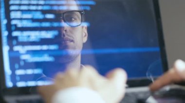 Gözlükadam Hacker Programcı Çift Pozlama Shot bir dizüstü bilgisayarda çalışıyor. Monitörde Yansıma: Geliştirici mavi kod yazıyor ve Lezzetli Kahve İçme.