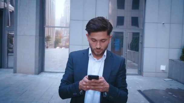 Genç İş Adamı Big City Business District Caddesi'nde Yürürken Akıllı Telefon Kullanır. Klasik giyinmiş. Arka planda Büyük Ofis Binası. Başarılı, Kendinden Emin Görünmek. — Stok video