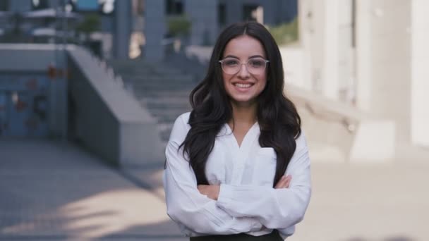 Portret młodej udanej bizneswoman w okularach stojących w pobliżu nowoczesnego biurowego budynku patrząc na kamerę i uśmiechając 4K — Wideo stockowe