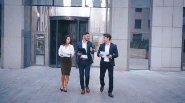 Başarılı İş Adamları İş Tartışmak ve Central Business District yürümek. İki Genç Erkek ve Takım Elbiseli Bir Kadın İletişim ve İş Merkezi Ofis Binası yakınında yürümek.
