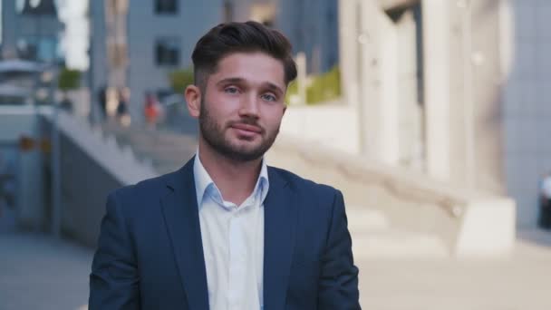 Retrato de un exitoso joven hombre de negocios en traje de pie en la ciudad cerca del centro de negocios disfrutando de un estilo de vida urbano profesional. Hombre guapo empleado mirando a la cámara . — Vídeo de stock