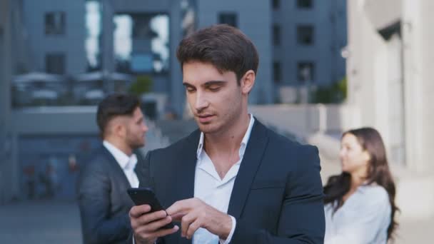 Handsome Businessman Using App on his Smartphone on Streets of Business District. Kontroluji zprávy, Mails. Vypadáš sebevědomě, úspěšně. Oblek oblečený. — Stock video