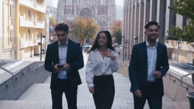 Başarılı İş Adamları İş Tartışmak ve Central Business District yürümek. İki Genç Erkek ve Takım Elbiseli Bir Kadın İletişim ve İş Merkezi Ofis Binası yakınında yürümek.