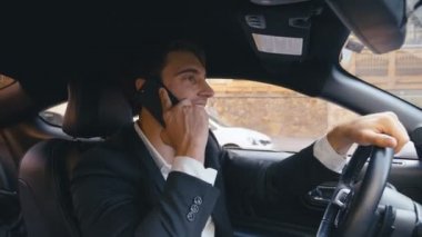 Meşgul İşadamı Araba Sürüyor ve Cep Telefonu'yla konuşuyor. Genç Kendine Güvenen Bir Adamın Portresi Araba Kullanıyor ve Şehirde Akıllı Telefon Kullanıyor.