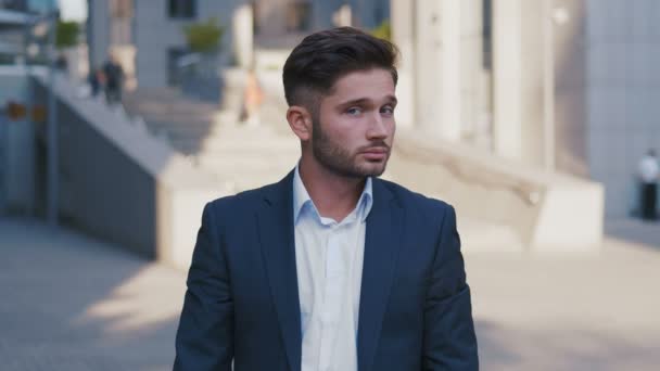 Portrait of successful young businessman in suit standing in city near business center enjoying professional urban lifestyle. Handsome male employee looking at camera. — Stock Video