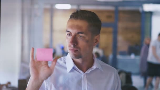 Junger Mann beim Brainstorming von Ideen in modernen Glasbüros. gutaussehender Geschäftsmann klebt eine klebrige Note auf Glasplatte — Stockvideo