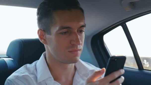 Der junge Geschäftsmann benutzt sein Smartphone während einer Autofahrt mit einem Fahrer. Mann checkt im Taxi Mails, Chats oder das Neue im Internet — Stockvideo