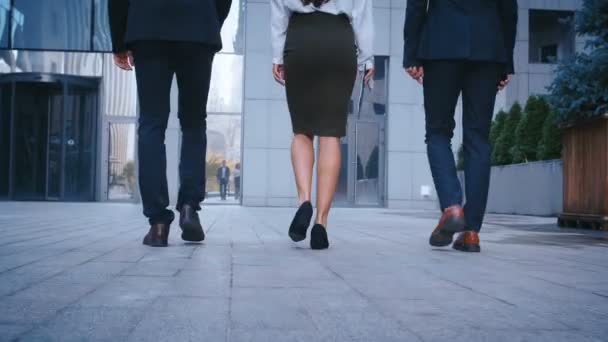 Rückseite Füße von drei erfolgreichen Geschäftsleuten, die zur Arbeit ins Bürogebäude pendeln. Geschäftsleute und Geschäftsfrauen in Anzügen gehen im Freien in die Stadt. — Stockvideo