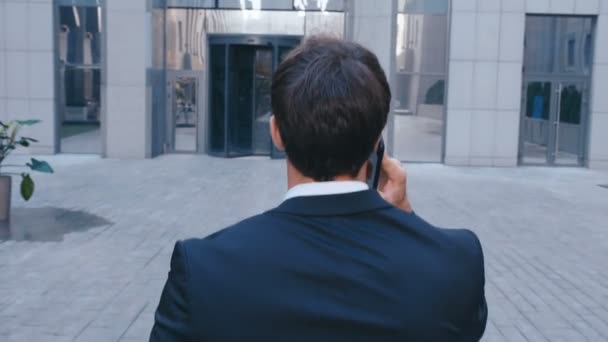 Visão traseira confiante empresário falando o telefone e andando na rua no centro do escritório. Conceito: tecnologia, telefonia, viagens de negócios, negócios . — Vídeo de Stock