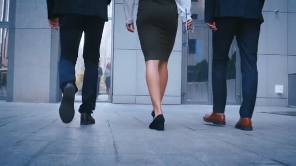 Nohy tří obchodních lidí dojímají do práce. Podnikatelé a obchodníci jdou do budovy kanceláře. Pohled zpět na kolegy, kteří jdou do města venku. — Stock video