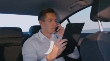 Genç İş adamı Sürücü ile Bir Arabada Rides ve Onun Cep Telefonu İstatistikve İş Sonuçları Tartışmak.