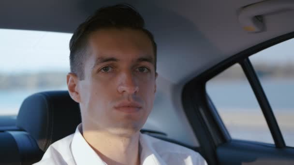 Close-up portret van zakenman reizen in een auto met een chauffeur. Jonge man in wit overhemd rijdt in een taxi — Stockvideo