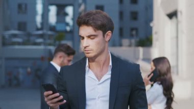 Akıllı Telefon ve arka planda iş tartışırken iş adamları grubu kullanarak Genç Adam Portresi. Merkez İş Bölgesi'nde çalışıyor. Klasik Takım Elbise Giymek.