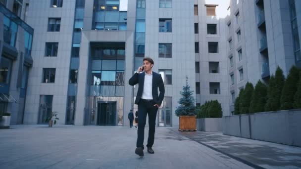 Uomo d'affari di successo Camminando per le strade del quartiere degli affari e parlando sul telefono cellulare. Fiducioso uomo caucasico attraente in tuta camminare fuori vicino a grande edificio per uffici e utilizzando smartphone . — Video Stock