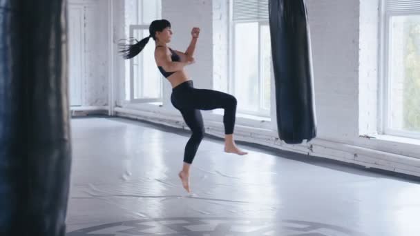 テコンドーのプロアスリートの女性がジムでパンチバッグを蹴る。ジムでアスレチックキックボクシング女子トレーニング. — ストック動画