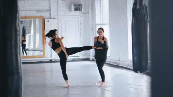 Atletische vrouw traint haar kicks op een punching tas die haar partner houdt. Training van Taekwondo of kickboxing. Twee Sportswomen training in Gym — Stockvideo