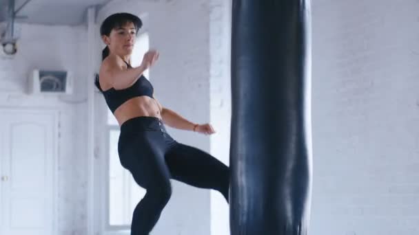 Taekwondo athlète professionnelle femme donne un coup de pied dans le sac de coups de poing dans la salle de gym. Kickboxing athlétique femme s'entraînant dans la salle de gym . — Video