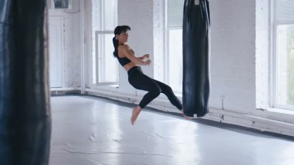 Taekwondo athlète professionnelle femme donne un coup de pied dans le sac de coups de poing dans la salle de gym. Kickboxing athlétique femme s'entraînant dans la salle de gym . — Video