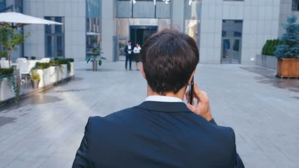 Cep telefonuyla konuşurken ofis yakınında yürüyen beyaz bir işadamının arka görüntüsü. — Stok video
