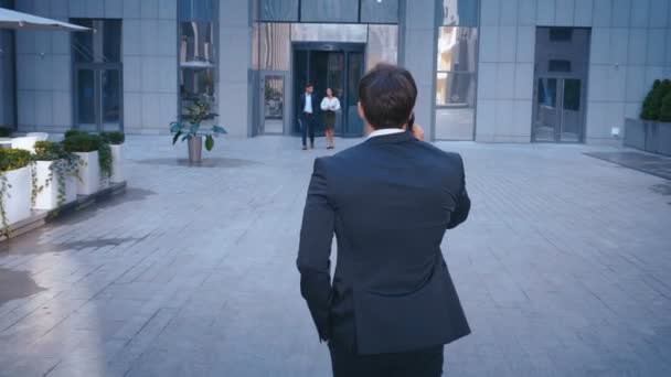 Visão traseira do empresário caucasiano bem sucedido em terno andando na rua no centro do escritório e falando ao telefone . — Vídeo de Stock