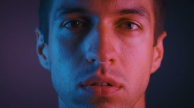 Neon ışıklar da yüzünde ciddi ve kendinden emin ifade ile kameraya bakan yakışıklı genç adamın portresi.