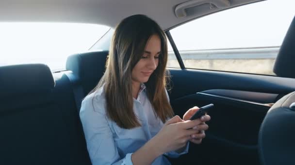 Портрет молодой женщины с помощью смартфона во время путешествия в автомобиле с водителем. Девушка проверяет почту, чаты, пока едет на такси — стоковое видео