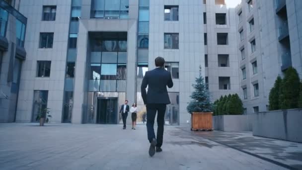 Vista trasera del exitoso hombre de negocios caucásico en traje caminando por la calle en el centro de oficinas y hablando por teléfono . — Vídeos de Stock