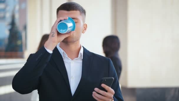 Empresario bien vestido junto a su oficina. Beber café para llevar. Escribir mensaje en su teléfono inteligente. Comunicación de personas en segundo plano. Distrito de negocios . — Vídeo de stock