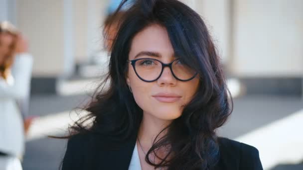 Retrato de una joven y bonita mujer de negocios con anteojos cerca del moderno edificio de oficinas. Chica mirando a la cámara y sonriendo . — Vídeo de stock