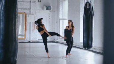 Atletik Kadın, Partnerinin Tuttuğu Kum Torbasına Tekmelerini Yetiştiriyor. Taekwondo veya Kickboks eğitimi. Spor Salonunda İki Sporcu Kadın Eğitimi