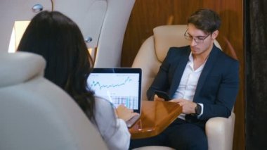 Başarılı iş adamları özel jet kullanıyor. Dizüstü bilgisayarda çalışıyorum. Akıllı telefon kullanıyordu. İş adamı ve iş kadını birinci sınıf bir uçakla uçuyor..