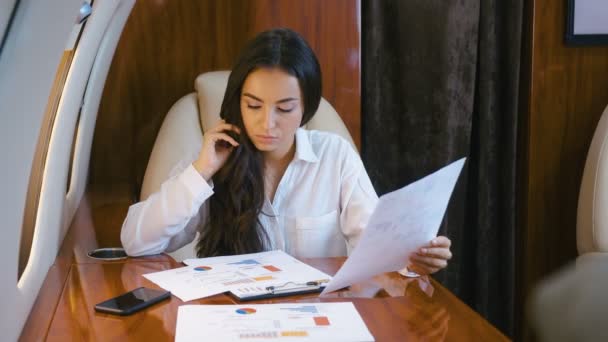 Een rijke vrouw die in een privéjet reist. Drukke zakenvrouw vliegt in een vliegtuig in business class. Werken met documenten, bestuderen van verkoopschema 's. — Stockvideo