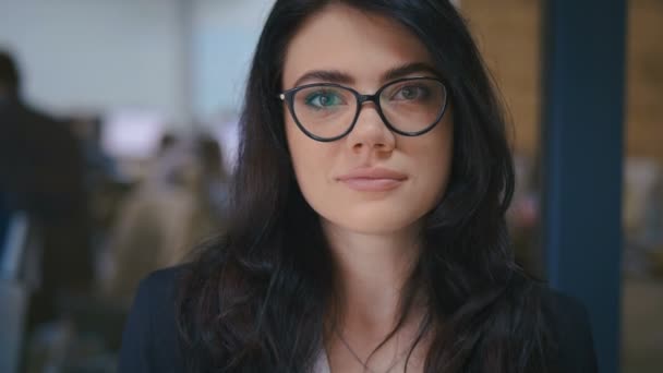 Belle jeune femme brune confiante joli visage regardant la caméra au bureau, portrait rapproché. Je porte des lunettes. Travaux de bureau sur le fond . — Video