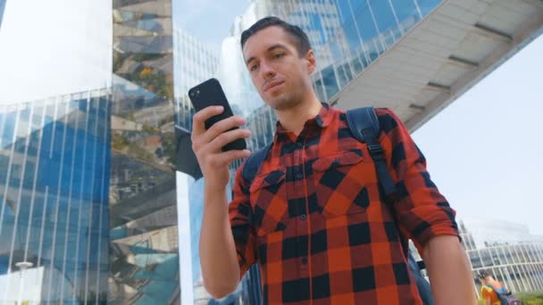 Κοντινό πλάνο νεαρός άνδρας χρησιμοποιούν το τηλέφωνο στην πόλη. Tourist σε κόκκινο πουκάμισο χρησιμοποιώντας samrtphone σε γυαλί εκτυφλωτικό φόντο. — Αρχείο Βίντεο