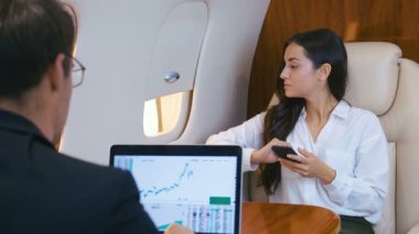 Başarılı iş adamları özel jet kullanıyor. Dizüstü bilgisayarda çalışıyorum. Akıllı telefon kullanıyordu. İş adamı ve iş kadını birinci sınıf bir uçakla uçuyor..