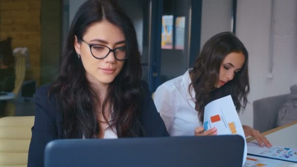 Geschäftsfrau, die glücklich lächelt und im Büro in die Kamera blickt. junge Frau arbeitet mit Laptop am Schreibtisch in modernem Büro. — Stockvideo