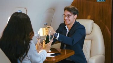 Grup iş adamları bir şişe şampanyayla kutlama yapıyor ve özel jet uçağıyla uçarken başarılarını kutluyorlar..