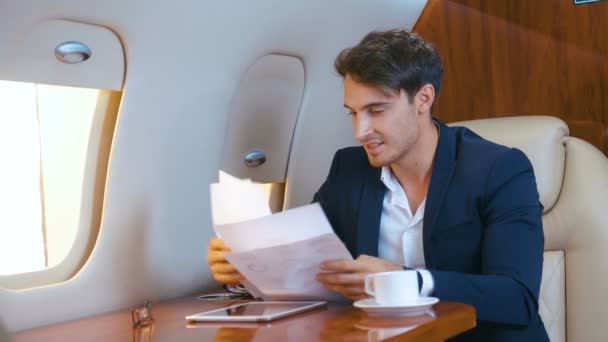 L'uomo sicuro di sé in giacca e cravatta getta documenti di lavoro e gode del successo e della vittoria negli affari durante un volo su un aereo jet privato. Il concetto di vincere. Concetto di successo . — Video Stock