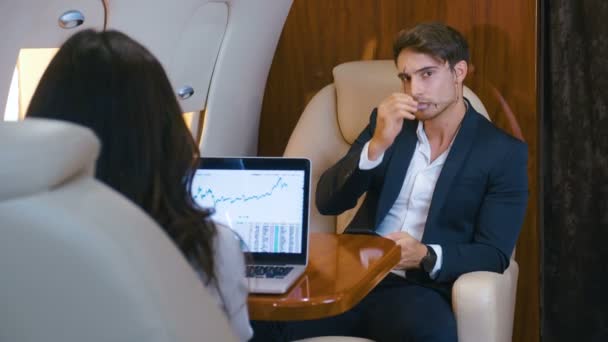 Des gens d'affaires prospères pilotent un jet privé. Travailler à l'ordinateur portable. Utilisation d'un smartphone. Homme d'affaires et femme d'affaires volant dans la première classe d'un avion . — Video