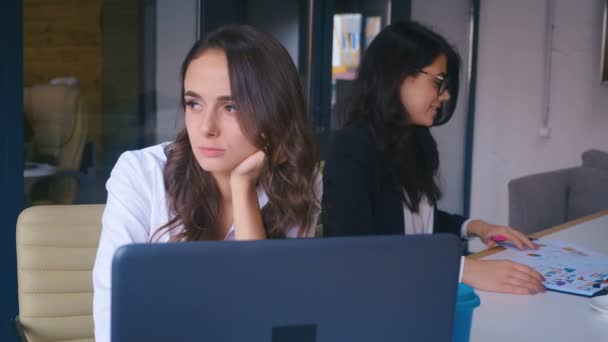 Znudzona bizneswoman siedząca przy laptopie w biurze. Zmęczona kobieta w depresji, próbująca pracować przy współpracownikach. Koncepcja - trudności w pracy. — Wideo stockowe