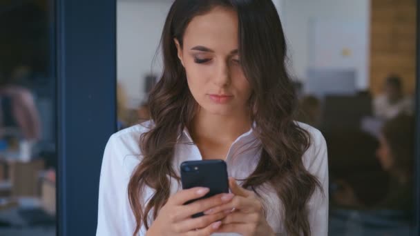 バックグラウンドでオフィス内のスマートフォンのメッセージを持つ美しい若いビジネス女性の閉鎖 — ストック動画