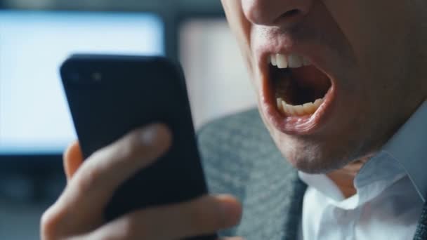 Homme d'affaires agressif parlant sur un appel vidéo sur un téléphone portable. L'homme crie furieusement et montre de l'agressivité à l'interlocuteur. Fond de bureau. Stress au travail . — Video