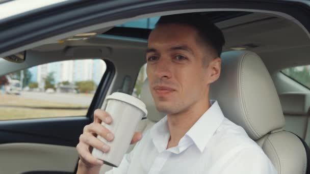 穿着白衬衫的年轻商人坐在司机座位上的汽车里，喝着美味的咖啡. — 图库视频影像