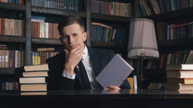 Klasik takım elbiseli bir işadamı kütüphanede oturmuş kitaplarda bilgi arıyor.