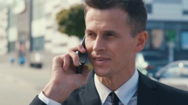 Kapalı çekim gülümseyen iş adamı dışarıda cep telefonundan konuşuyor. Ofis geçmişine telefon eden neşeli iş adamlarına yakın çekim. Klasik takım elbise giyiyor..