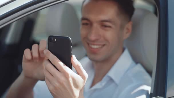 Портрет усміхненого чоловіка бізнесмена в білій сорочці, що сидить за кермом автомобіля і використовує смартфон. Водій за допомогою мобільного телефону . — стокове відео