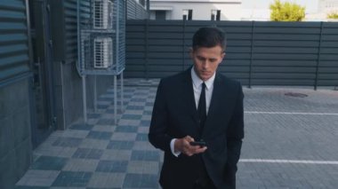 Takım elbiseli, kendine güvenen iş adamının telefonuyla yürümesinin yan görüntüsü. Dışarıdaki akıllı telefona bakan bir adam.
