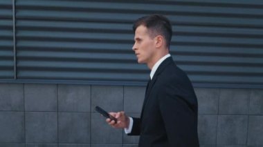 Cep telefonu kullanan kendine güvenen bir iş adamı. Takım elbiseli genç adam mesaj atıyor, Ofis Bölgesi 'nde yürürken akıllı telefonunu aldatıyor. İş için. Sosyal ağ. - İnsanlar. Uygulamalar.